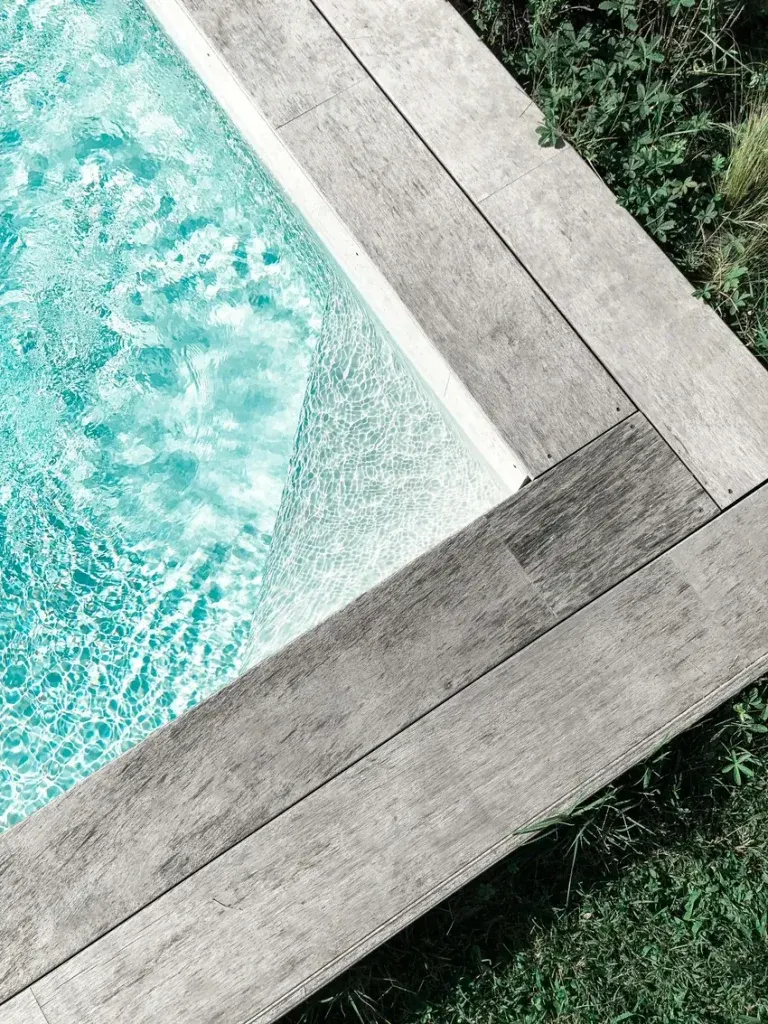 Sunlit turquoise swimming pool water beside pale decking