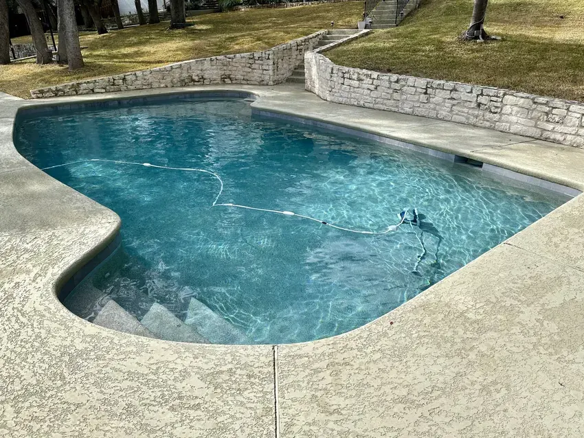 Curved backyard swimming pool beside a stone water feature