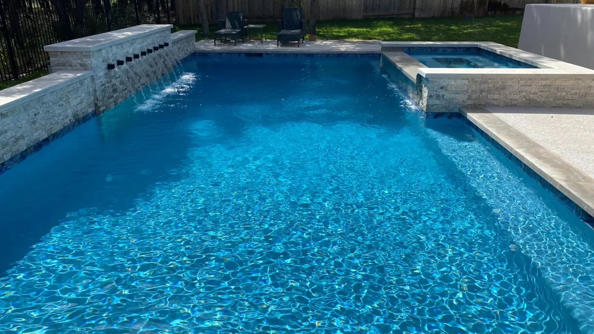 Sunlit residential swimming pool with clear blue water and surrounding greenery